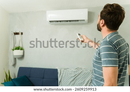 Man using a remote control, adjusting the temperature of his minisplit air conditioning unit during a hot summer day