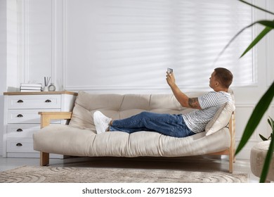 Man using remote to control air conditioner on sofa at home
