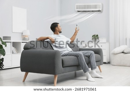 Man using remote to control air conditioner on sofa at home