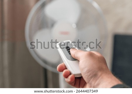 Man using remote control to turn on or off floor fan in room.