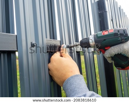 A man using a screwdriver twists a metal picket fence on the fence. Worker, professional, construction. Fencing, security, own territory
