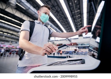 Man using self service check-in machine. Passenger scanning ticket on smart phone at airport terminal. Selective focus on hand holding smartphone.