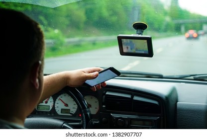 Man Using A Smart Phone Sitting On The Front Seat Of The Car. Back View Focused On The Screen. 