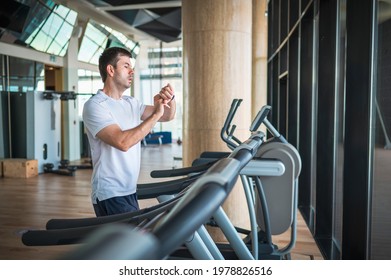 Man Using Smart Watch Fitness Tracker Device While Jogging On A Treadmill During A Cardio Running Warmup Exercise In The Gym For Staying Fit And In Shape With Healthy Lifestyle