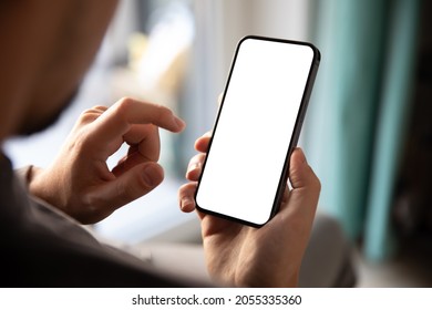 Man using smartphone blank screen frameless modern design while sitting on the chair in home interior - Shutterstock ID 2055335360