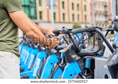 Man using smartphone at city bike-sharing station with blue bicycles