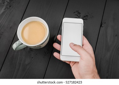 Man using smartphone, close-up, cup of coffee and on the balck wooden background. Top view.