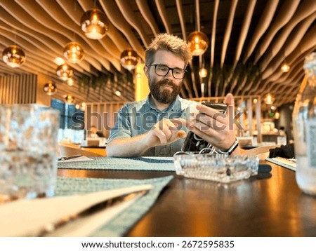 Man using smartphone at dining table in restaurant. Lifestyle, communication, leisure and casual technology interaction within modern dining interior and social atmosphere.
