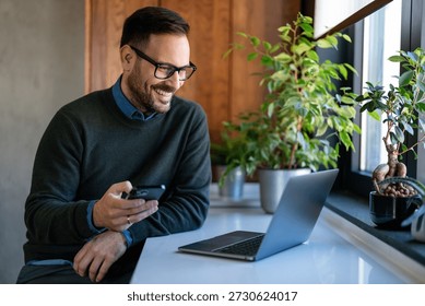 Man using smartphone and laptop computer for electronic banking, making reservation, online shopping