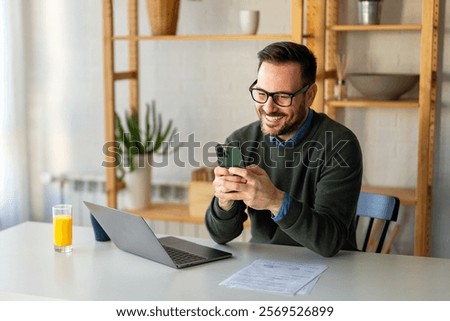 Man using smartphone and laptop computer for electronic banking, making reservation, online shopping