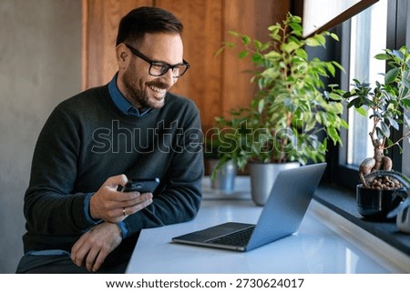 Man using smartphone and laptop computer for electronic banking, making reservation, online shopping