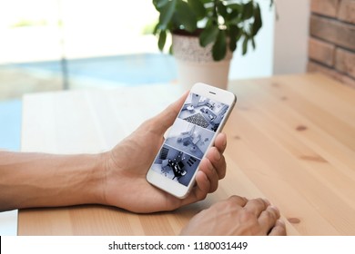 Man Using Smartphone For Monitoring CCTV Cameras At Table Indoors. Home Security System