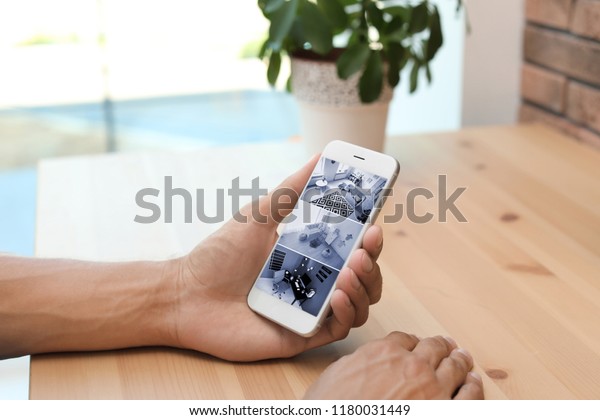Man using smartphone for monitoring CCTV
cameras at table indoors. Home security
system