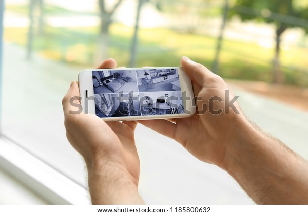Man using smartphone for monitoring CCTV cameras\
indoors. Home security\
system