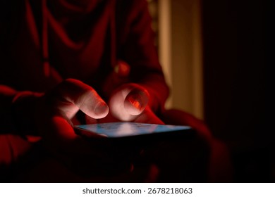 Man using smartphone at night. Close up of hand holding smartphone, swiping and scrolling social media feed on glowing screen in dark room