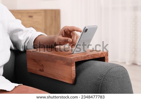 Man using smartphone on sofa armrest wooden table at home, closeup