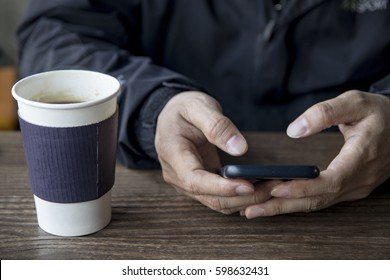 a man is using the smartphone on the table next to a cup of coffee