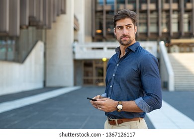 Man using smartphone outdoor. Portrait of young businessman using mobile phone while looking away on the street. Thoughtful business man in blue formal clothing using cellphone outside office building - Powered by Shutterstock