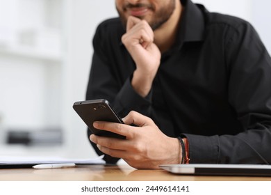 Man using smartphone at table in office, closeup