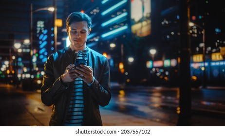 Man Using Smartphone Walking Through Night City Street Full of Neon Light. Smiling Stylish Man Using Mobile Phone, Social Media, Online Shopping, Texting on Dating App. - Powered by Shutterstock