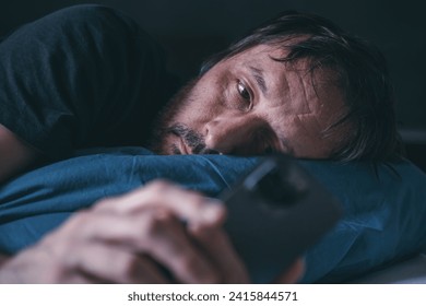 Man using smartphone while lying in the bed late at night, insomnia concept, selective focus