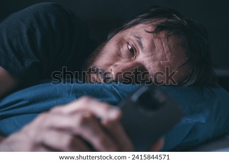 Man using smartphone while lying in the bed late at night, insomnia concept, selective focus