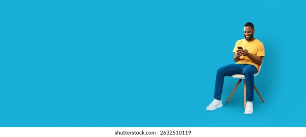 Man using smartphone while sitting on chair against blue background