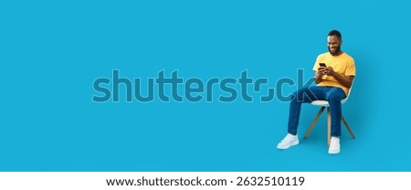 Man using smartphone while sitting on chair against blue background