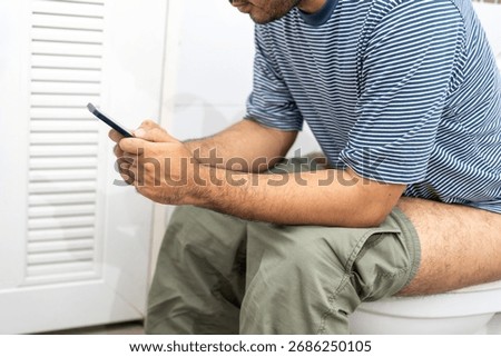 Man using smartphone while sitting on toilet bowl in bathroom at home.
