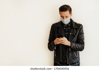 Man using smartphone while wearing surgical mask near white wall. Health, epidemics, social media, communication and lifestyle stills with copy space. Men wear masks to prevent air pollution.