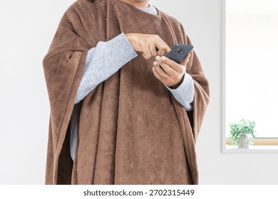 A man using a smartphone while wearing a wearable blanket (30s, Japanese, faceless)