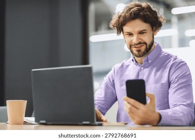 Man Using Smartphone While Working on Laptop in Office During Daytime