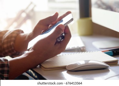 Man using Smartphone while working on desk with blurred office background.	

