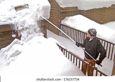 Man Using A Snow Rake On Garage Roof In Winter