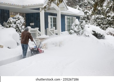 Man using snowblower to clear deep snow on driveway near residential house after heavy snowfall - Powered by Shutterstock