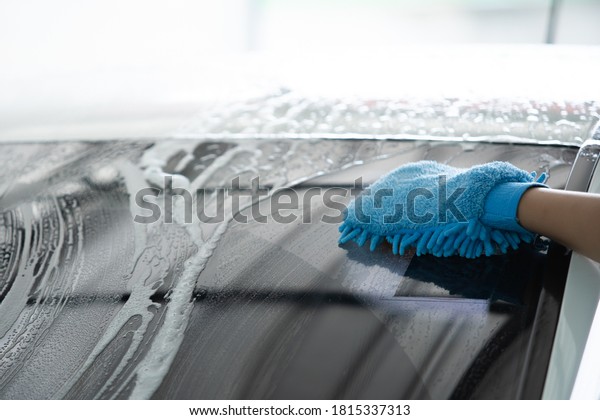 Man using a\
sponge with car wash shampoo wiping on the windshield close up.\
Auto car and car wash service\
concept.