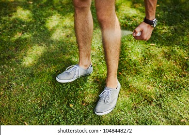 Man Using Spray Bottle Of Insect Repellent On His Leg Outdoors