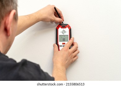 Man using stud finder to locate framing studs located behind the walling surface. Using a wall scanner to identify hidden electrical wiring. Space for text.