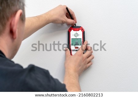 Man using a stud finder to locate framing studs located behind the walling surface. Using a wall scanner to identify hidden electrical wiring. Space for text.