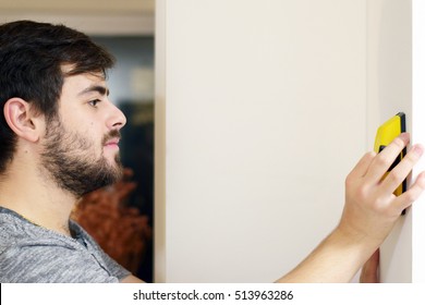 Man Using Stud Finder To Search Apartment Wall For Studs And Live Wires