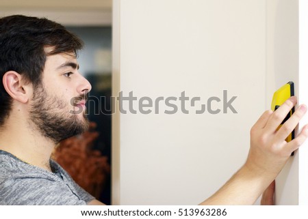 Man using stud finder to search apartment wall for studs and live wires