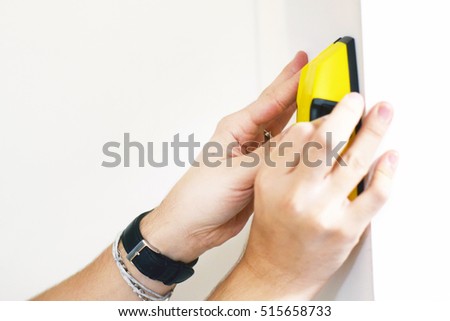 Man using stud finder to search apartment wall for studs and live wires