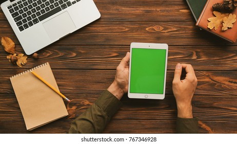 Man Using Tablet Computer On The Wooden Table With Laptop And Notebooks. Top View Shot. Male Finger Scrolling, Tapping On The Green Screen. Chroma Key. Vertical