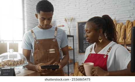 Man using tablet and woman holding coffee in a bakery, both wearing aprons, discussing business tasks in an indoor shop setting. - Powered by Shutterstock