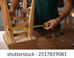 Man using tape measure while repairing wooden stool indoors, closeup