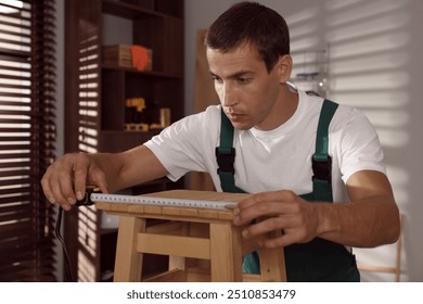 Man using tape measure while repairing wooden stool indoors