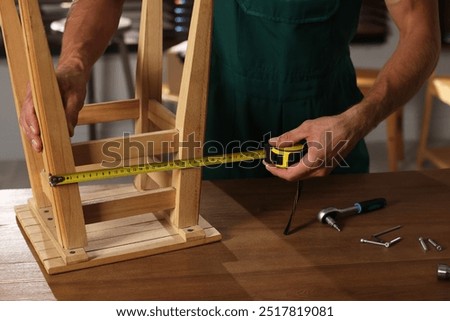 Man using tape measure while repairing wooden stool indoors, closeup