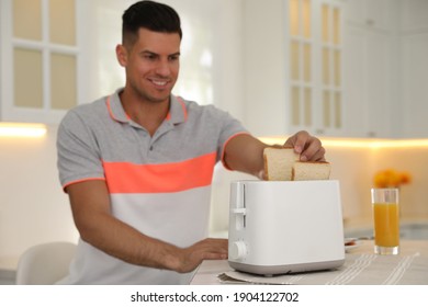 Man Using Toaster At Table In Kitchen