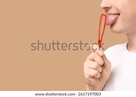 Man using tongue scraper on beige background, closeup