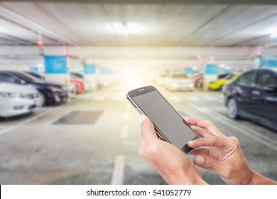 Man using touch screen mobile phone with blur cars parking